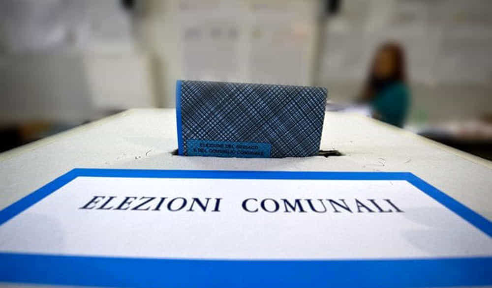 Si rappresenta un'urna elettorale, dove viene inserita una scheda elettorale. La scritta indica "ELEZIONI COMUNALI".