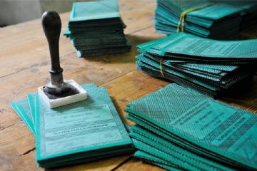 Tessere elettorali di colore verde sul tavolo, pronte per essere vidimate dagli scrutatori con apposito timbro appoggiato sulle tessere.